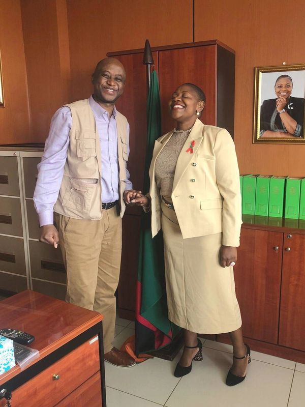 Two colleagues smiling and holding hands in an office setting.