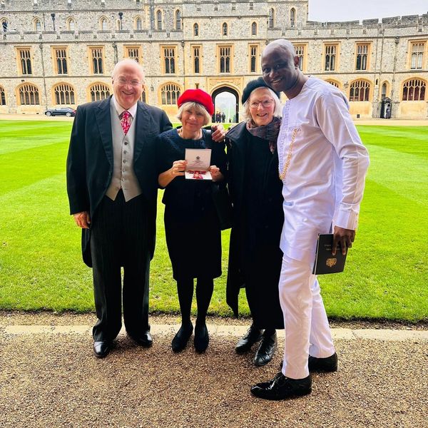 Four people posing happily outdoors in front of a grand building, one holding an award.